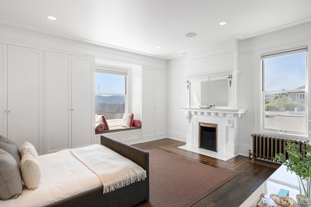 bedroom featuring radiator, baseboards, wood finished floors, ornamental molding, and a high end fireplace