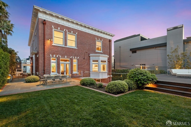 back of property with a lawn, brick siding, a deck, and a patio