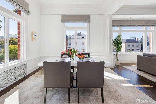 dining area featuring ornamental molding, wood finished floors, ornate columns, and a decorative wall