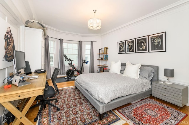 bedroom with wood-type flooring, ornamental molding, and an inviting chandelier