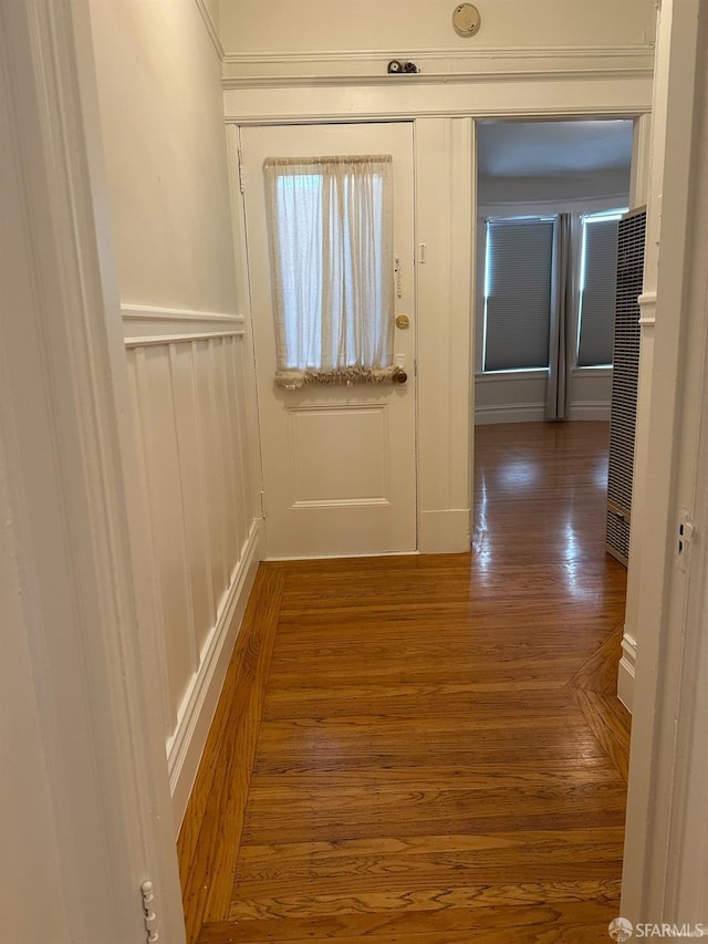 hallway with dark wood-style flooring, a wainscoted wall, and a decorative wall