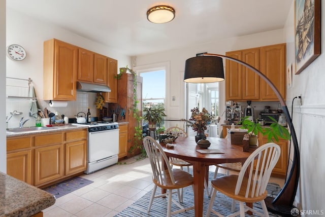 kitchen with white gas stove, under cabinet range hood, a sink, light countertops, and tasteful backsplash