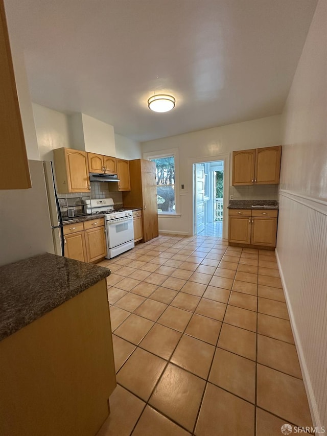 kitchen with light tile patterned floors, white range with gas cooktop, tasteful backsplash, freestanding refrigerator, and under cabinet range hood