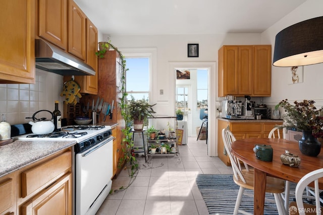 kitchen with light tile patterned floors, tasteful backsplash, white gas range, light countertops, and under cabinet range hood