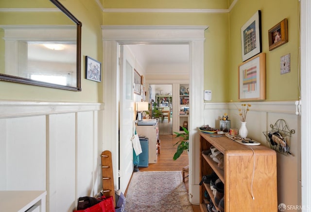 hall featuring ornamental molding, a wainscoted wall, a decorative wall, and wood finished floors