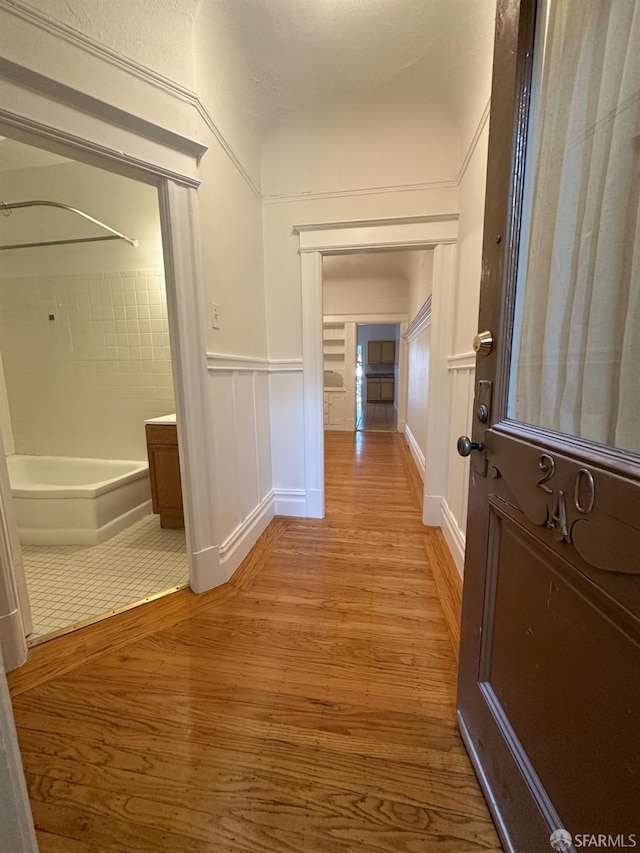 hallway with a wainscoted wall, wood finished floors, and a decorative wall