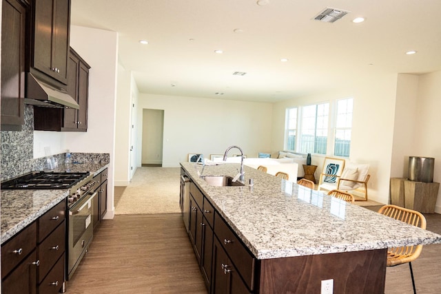 kitchen with a sink, a kitchen island with sink, a kitchen breakfast bar, high end stove, and under cabinet range hood
