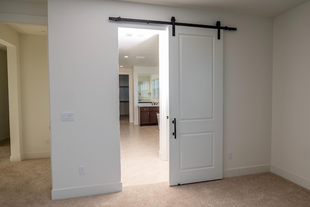 empty room with baseboards, a barn door, visible vents, and light carpet