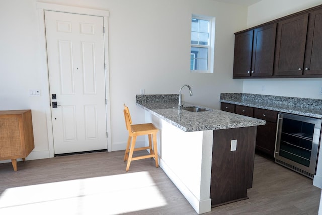 kitchen featuring dark brown cabinetry, light wood-type flooring, a sink, a peninsula, and wine cooler