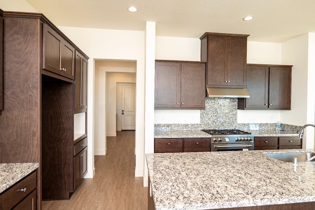 kitchen featuring dark brown cabinetry, under cabinet range hood, a sink, high end range, and light wood finished floors