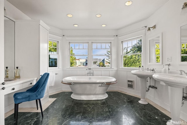 bathroom with a freestanding tub, recessed lighting, a decorative wall, a sink, and visible vents