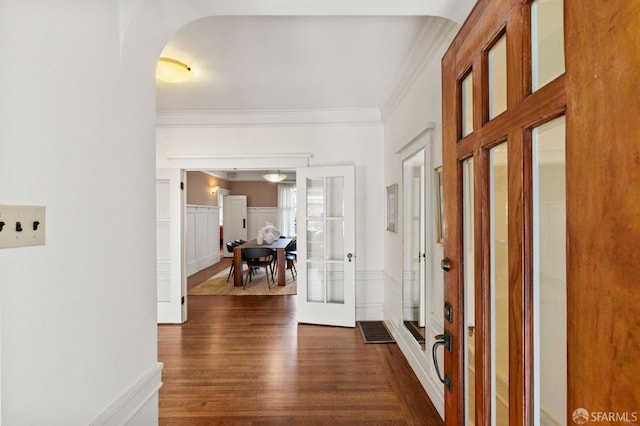 foyer entrance with arched walkways, french doors, a wainscoted wall, dark wood finished floors, and ornamental molding