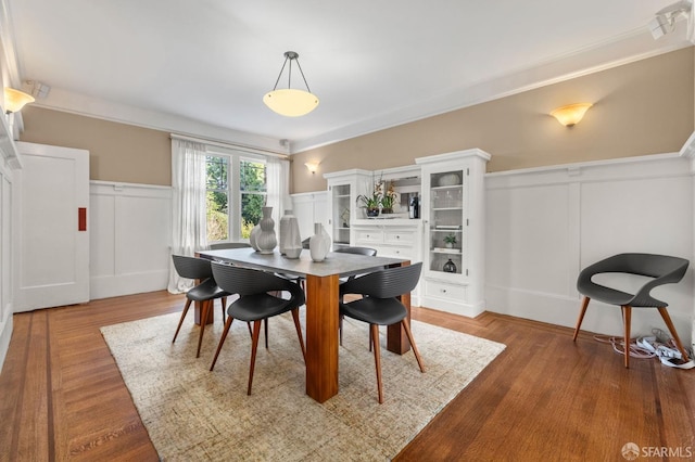 dining space featuring a wainscoted wall, ornamental molding, a decorative wall, and wood finished floors