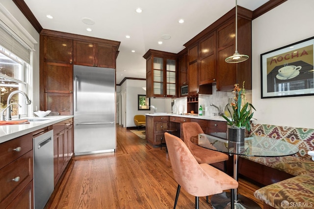 kitchen with stainless steel appliances, decorative backsplash, ornamental molding, a sink, and wood finished floors