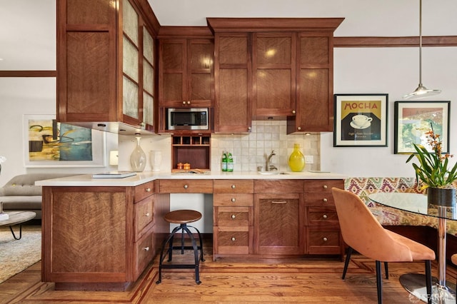 kitchen featuring a sink, light countertops, light wood finished floors, stainless steel microwave, and tasteful backsplash