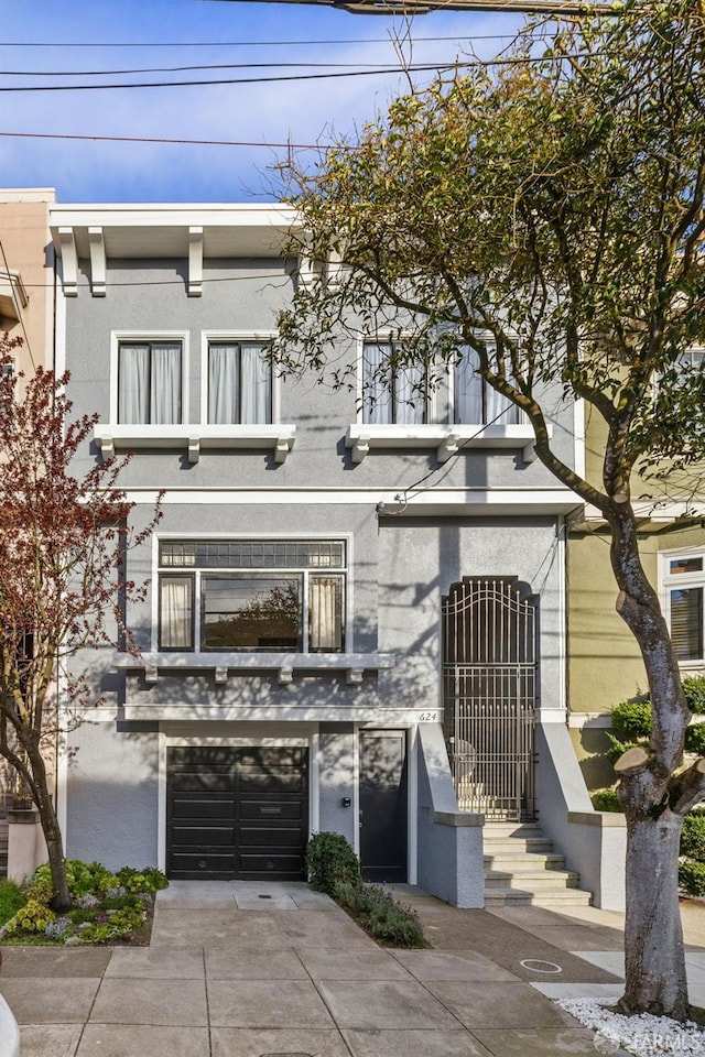 view of property with a garage, driveway, a balcony, and stucco siding