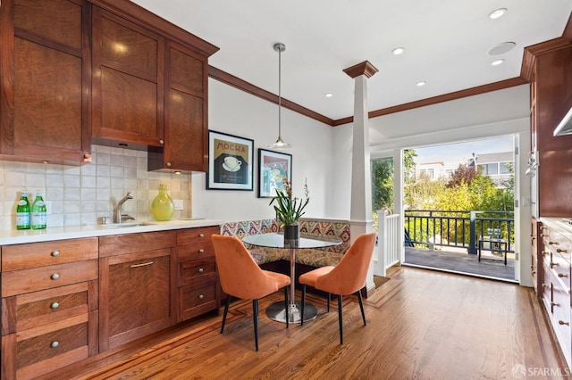 kitchen featuring wood finished floors, a sink, light countertops, ornamental molding, and decorative backsplash