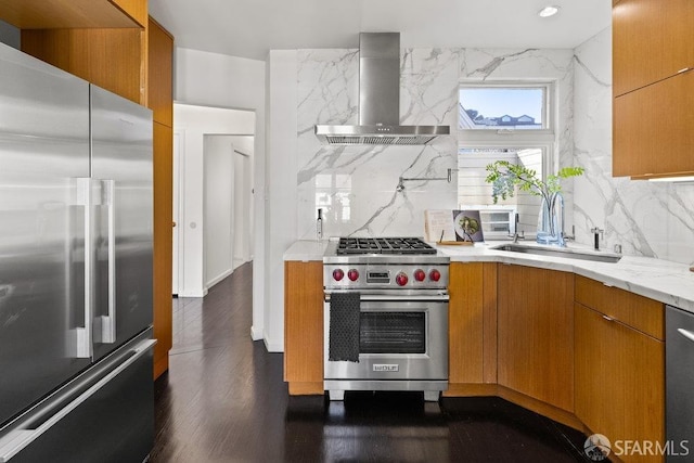 kitchen featuring high quality appliances, a sink, backsplash, dark wood finished floors, and wall chimney exhaust hood