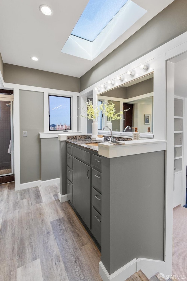 kitchen with light wood-style flooring, gray cabinets, a sink, a skylight, and light countertops