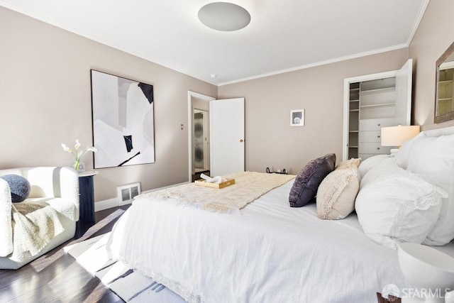 bedroom with wood finished floors, visible vents, baseboards, a walk in closet, and crown molding