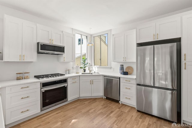 kitchen featuring stainless steel appliances, a sink, light wood-style floors, white cabinets, and light countertops