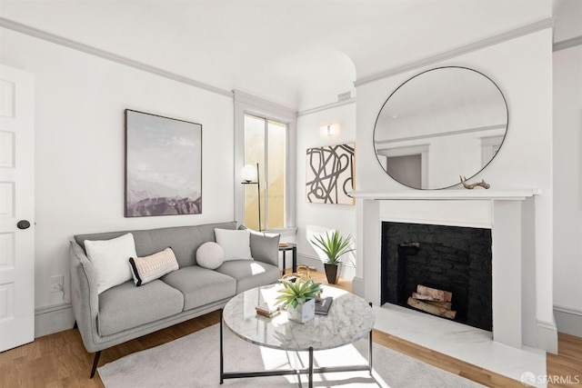 living area with visible vents, baseboards, a high end fireplace, light wood-type flooring, and crown molding