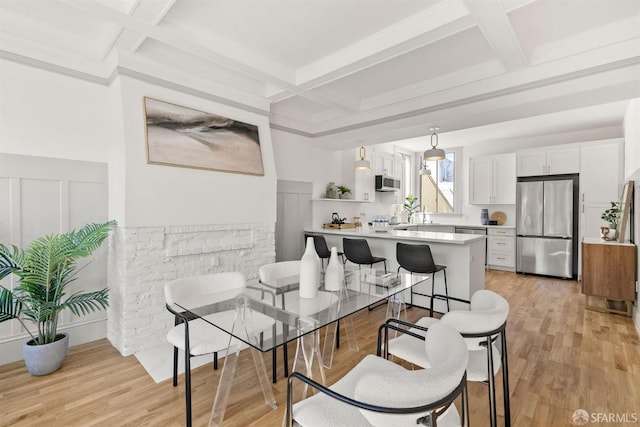 dining space with coffered ceiling, beamed ceiling, and light wood-style flooring