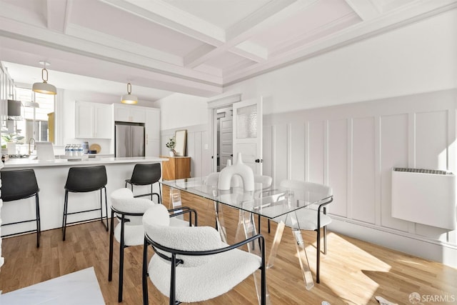 dining room featuring a decorative wall, a wainscoted wall, coffered ceiling, light wood-type flooring, and beamed ceiling