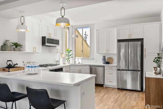 kitchen featuring light wood-style flooring, a peninsula, white cabinetry, light countertops, and appliances with stainless steel finishes