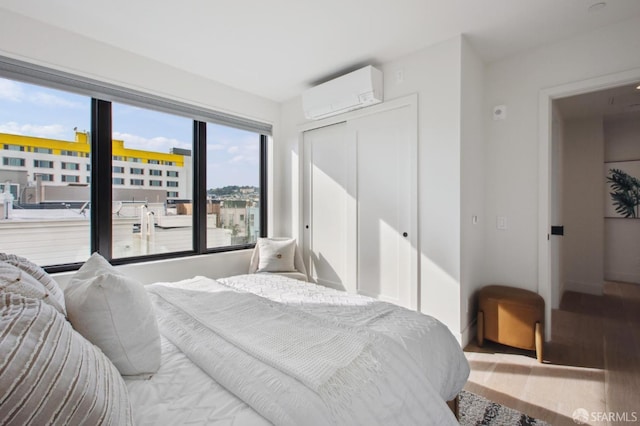 bedroom featuring wood finished floors, a wall mounted AC, a closet, and baseboards