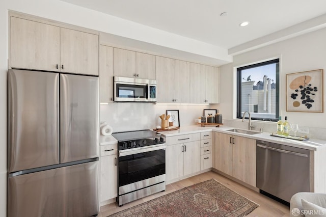 kitchen featuring light countertops, appliances with stainless steel finishes, light brown cabinets, a sink, and light wood-type flooring