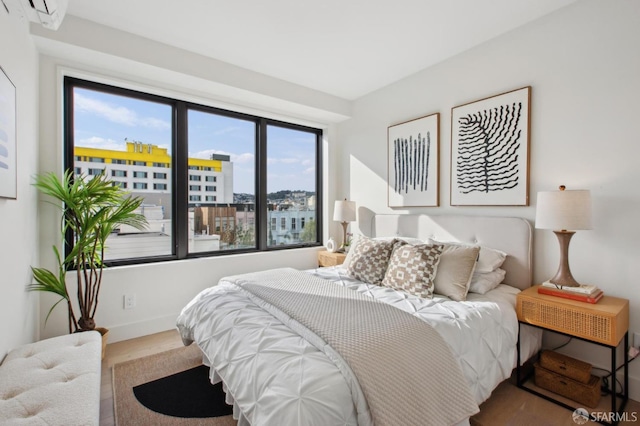 bedroom with a view of city, an AC wall unit, wood finished floors, and baseboards