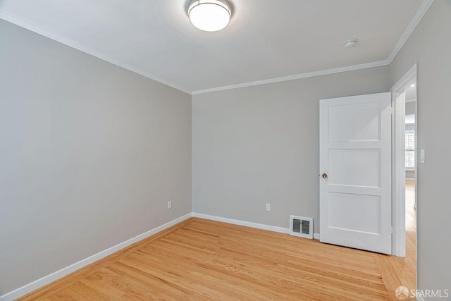 spare room with light wood-type flooring, baseboards, visible vents, and ornamental molding