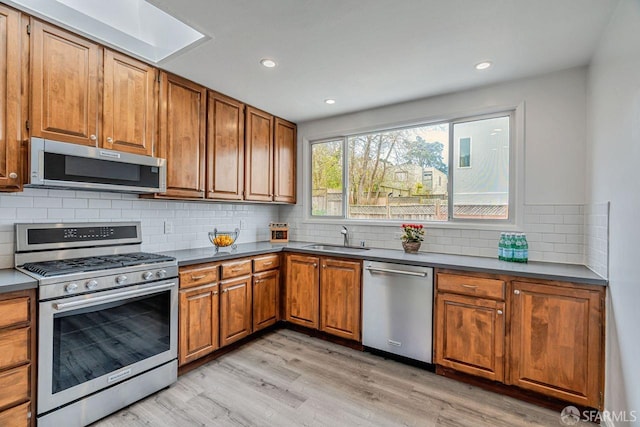 kitchen featuring stainless steel appliances, a sink, light wood-style floors, tasteful backsplash, and brown cabinetry