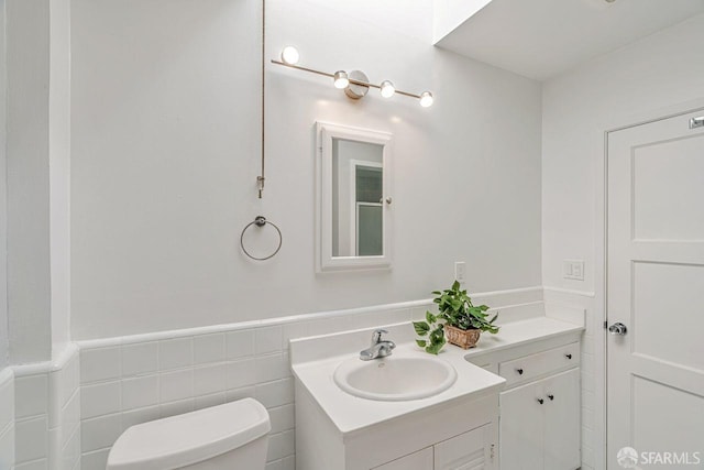 bathroom with toilet, a wainscoted wall, tile walls, and vanity