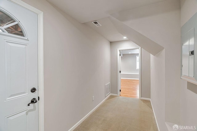 corridor featuring baseboards, electric panel, visible vents, and light colored carpet