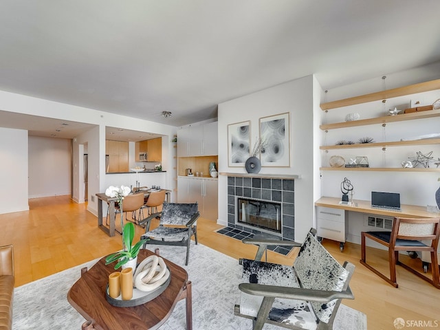 living room featuring light wood-type flooring, built in study area, and a tile fireplace