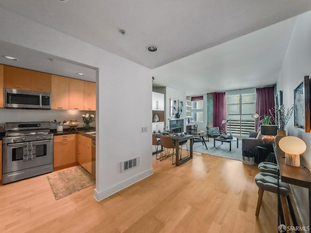 kitchen with stainless steel appliances, dark countertops, visible vents, and light wood finished floors