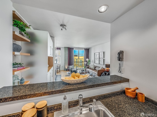 kitchen with dark countertops, white cabinetry, a sink, and open shelves