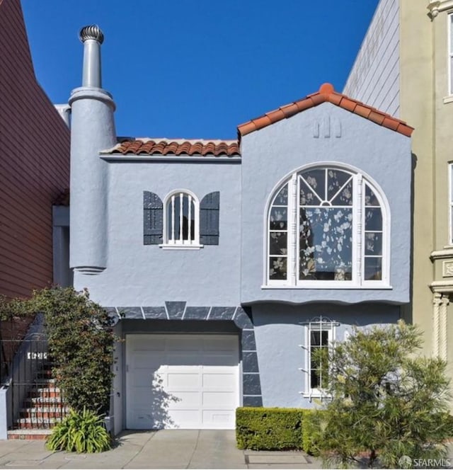 view of side of property featuring concrete driveway, a tile roof, and stucco siding