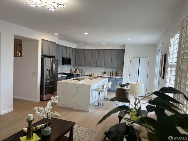 kitchen with appliances with stainless steel finishes, sink, gray cabinetry, a center island with sink, and light wood-type flooring