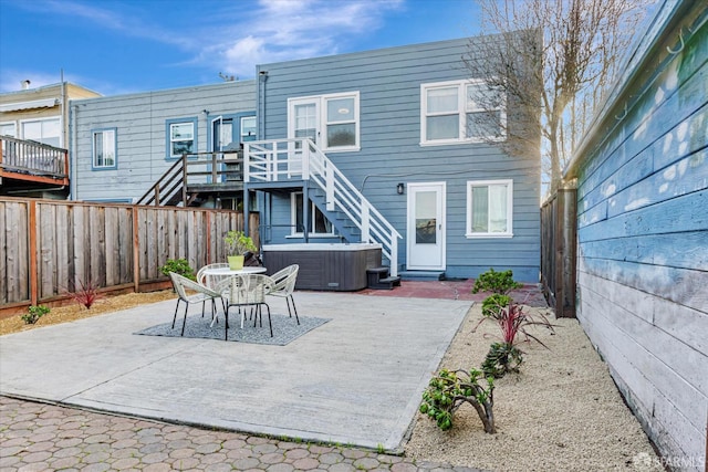 rear view of house featuring a hot tub, a wooden deck, a fenced backyard, and a patio