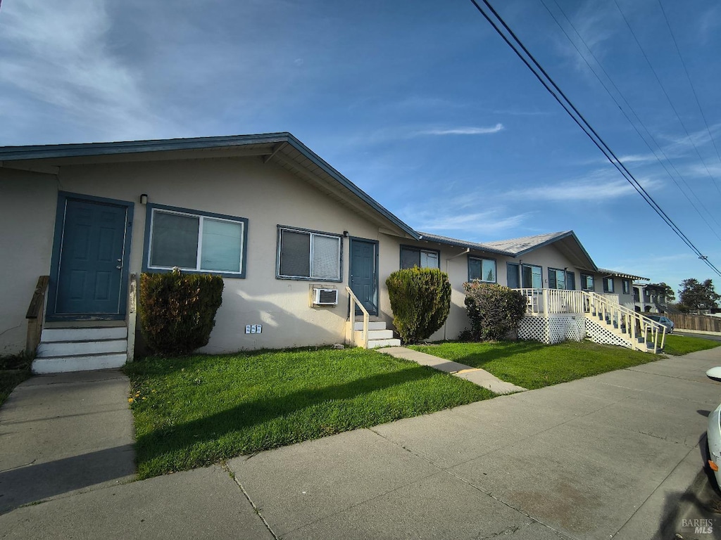 view of front of home featuring a wall unit AC and a front lawn