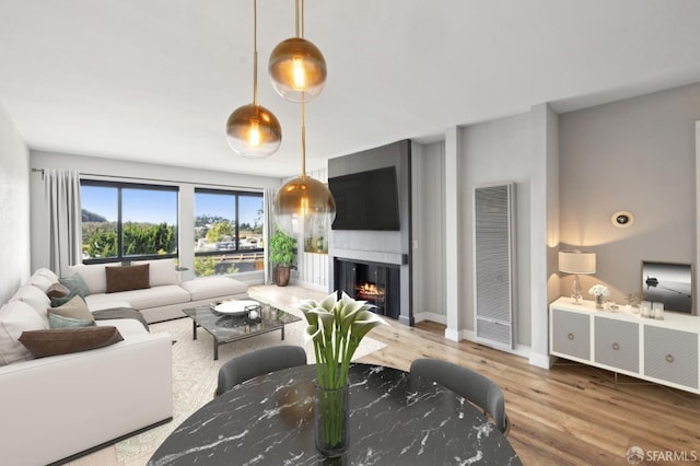 living area featuring a heating unit, wood finished floors, a warm lit fireplace, and baseboards