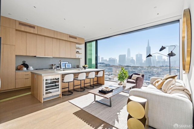 kitchen featuring light brown cabinetry, light hardwood / wood-style floors, wine cooler, and an island with sink