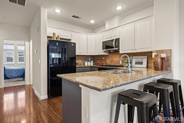 kitchen with a peninsula, stainless steel microwave, black refrigerator with ice dispenser, and visible vents