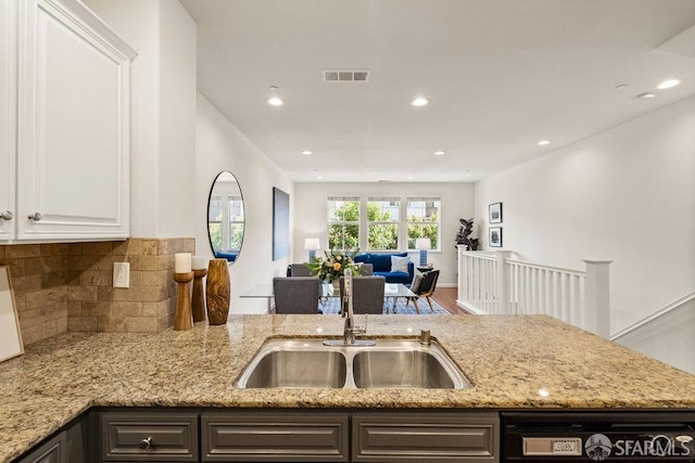 kitchen with visible vents, light stone countertops, a sink, open floor plan, and dishwashing machine