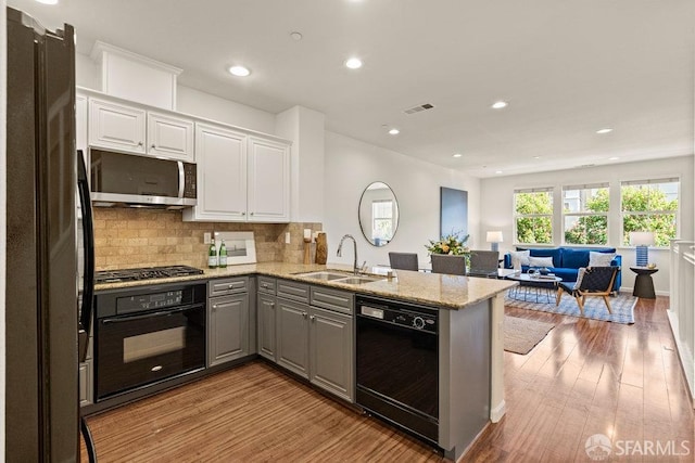 kitchen featuring a peninsula, gray cabinets, white cabinets, a sink, and black appliances