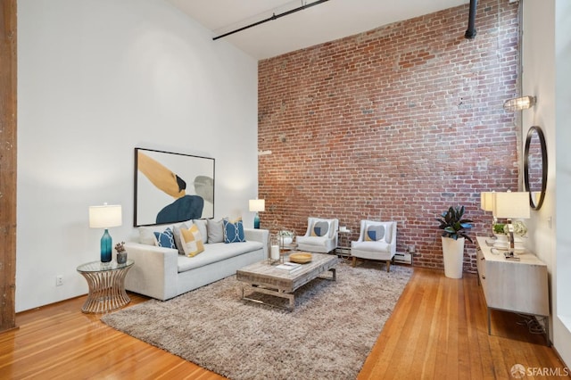 living room with a towering ceiling, hardwood / wood-style flooring, and brick wall