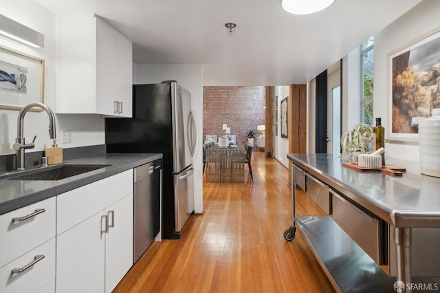 kitchen featuring white cabinetry, sink, stainless steel dishwasher, and brick wall